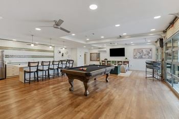 A pool table is in the middle of a room with a kitchen in the background.